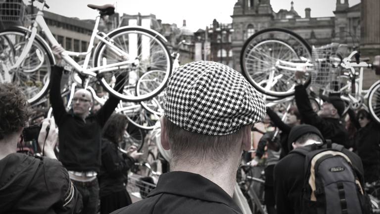 a group of people outside, holding up bicycles in the air 