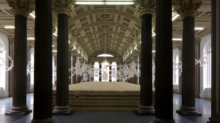 gallery installation, large pillars in foreground with view of sculptural works in background