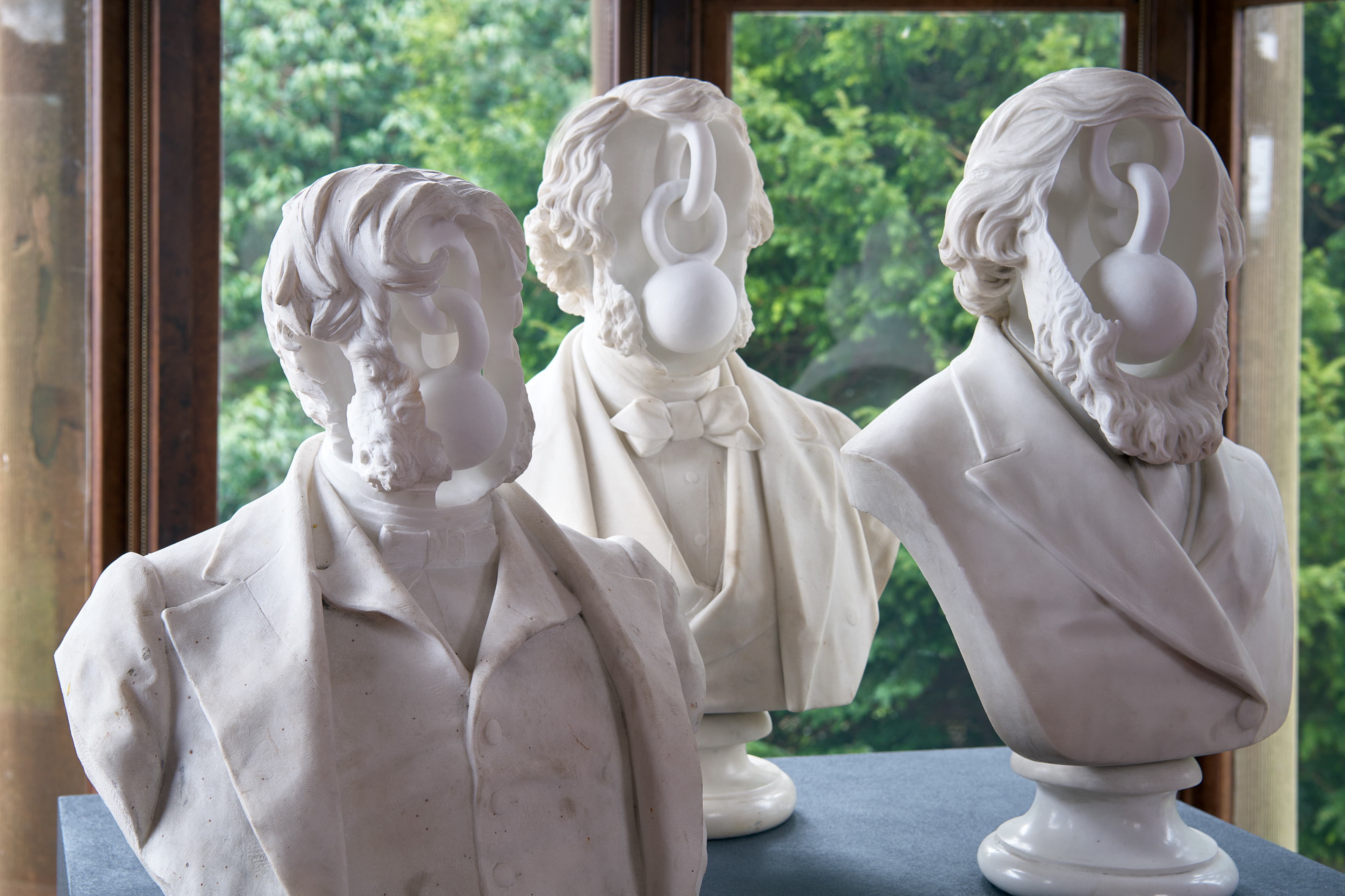 A close-up of three classical marble busts, each fitted with a smooth, faceless sculptural attachment obscuring their features, part of Jon Owen's installation at Holmwood House.