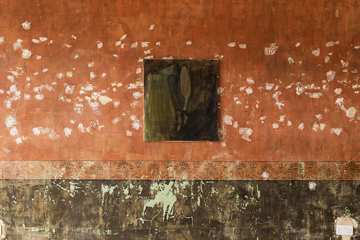 An abstract artwork featuring dark green colours is displayed on a wall of peeling paint.