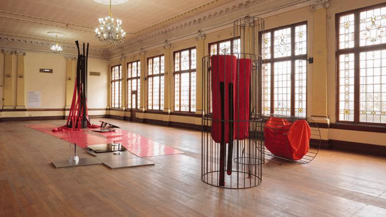 Installation view showing sculptural works against a long row of windows. Sculptures are made from a broad range of materials