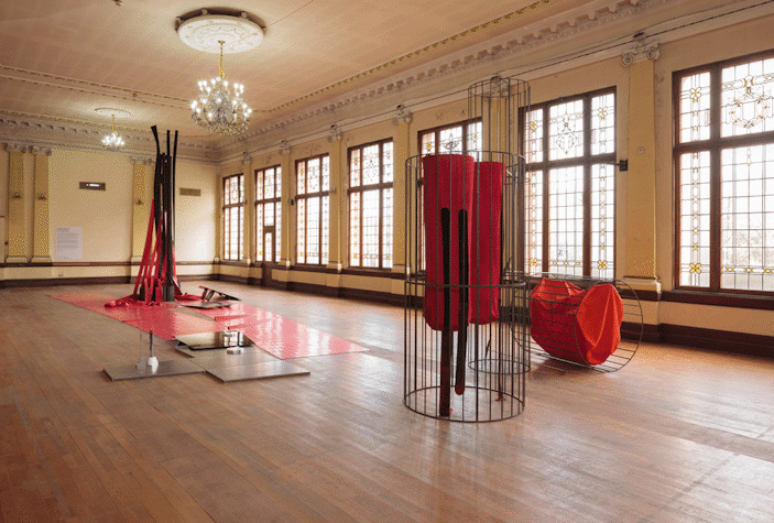 Installation view showing sculptural works against a long row of windows. Sculptures are made from a broad range of materials