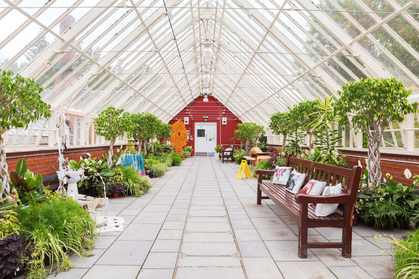 Interior view of glasshouse with plants, benches and some art work visible 