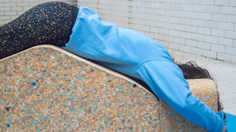 A person in a blue sweater lying over a block. Their head is partially hidden. The tiles of a swimming pool are visible in the background