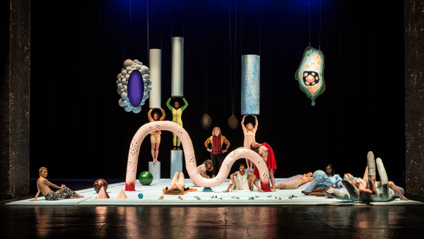 Horizontal, full view of Tai Shani's colorful art installation with people posing in Tramway as part of Glasgow International 2018.