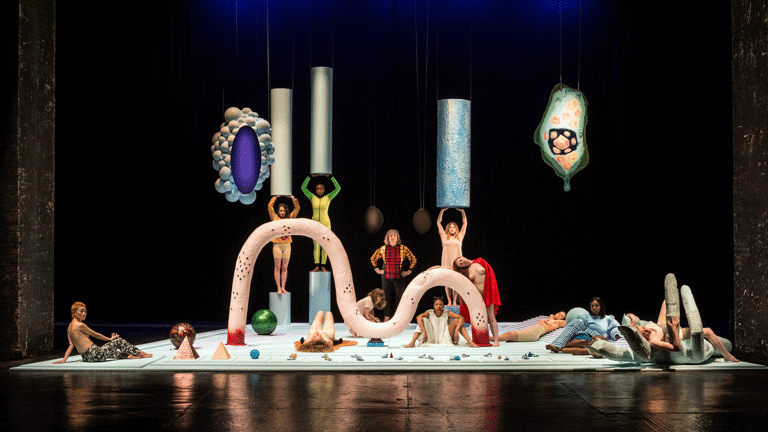 Horizontal, full view of Tai Shani's colorful art installation with people posing in Tramway as part of Glasgow International 2018.